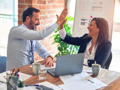Un homme et une femme d'affaires se congratulent avec un "high five" dans un bureau moderne, symbolisant la collaboration et le succès professionnel promus par Leaderseed.