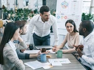 Un groupe de professionnels collaborant autour d’une table dans un espace moderne, avec des plantes en arrière-plan, illustrant les valeurs de collaboration, d’innovation et de durabilité de Leaderseed.