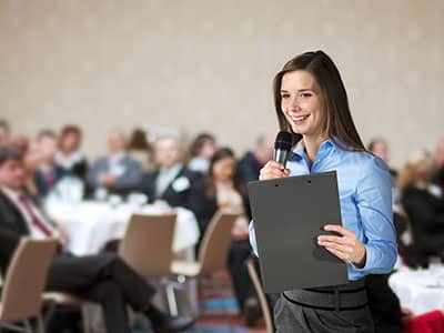 Manager souriante tenant un micro et s’adressant à une audience, illustrant les formations en développement personnel proposées par Leaderseed.