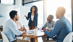 Jeune femme primo-manager dynamique souriant qui prouve sa valeur ajoutée en animant une réunion participative avec son équipe dans un espace de travail moderne.