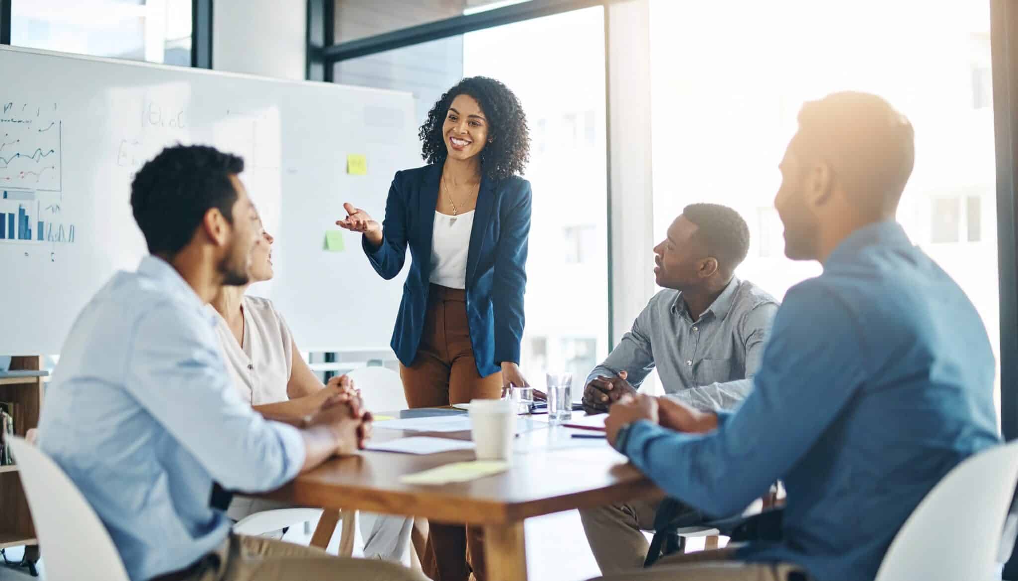 Réussir une bonne prise de poste : Jeune femme primo-manager dynamique souriant qui prouve sa valeur ajoutée en animant une réunion participative avec son équipe dans un espace de travail moderne.